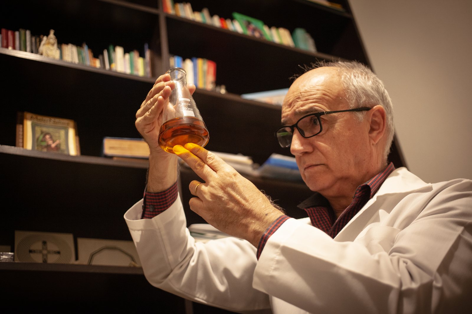 Prof. Rogério Fagundes Filho, de jaleco, examinando um frasco com preparado natural em seu consultório de pesquisa.