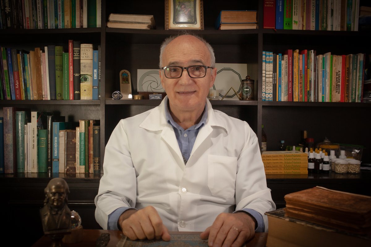 Prof. Rogério Fagundes Filho sentado em seu consultório, cercado por livros e preparados naturais.